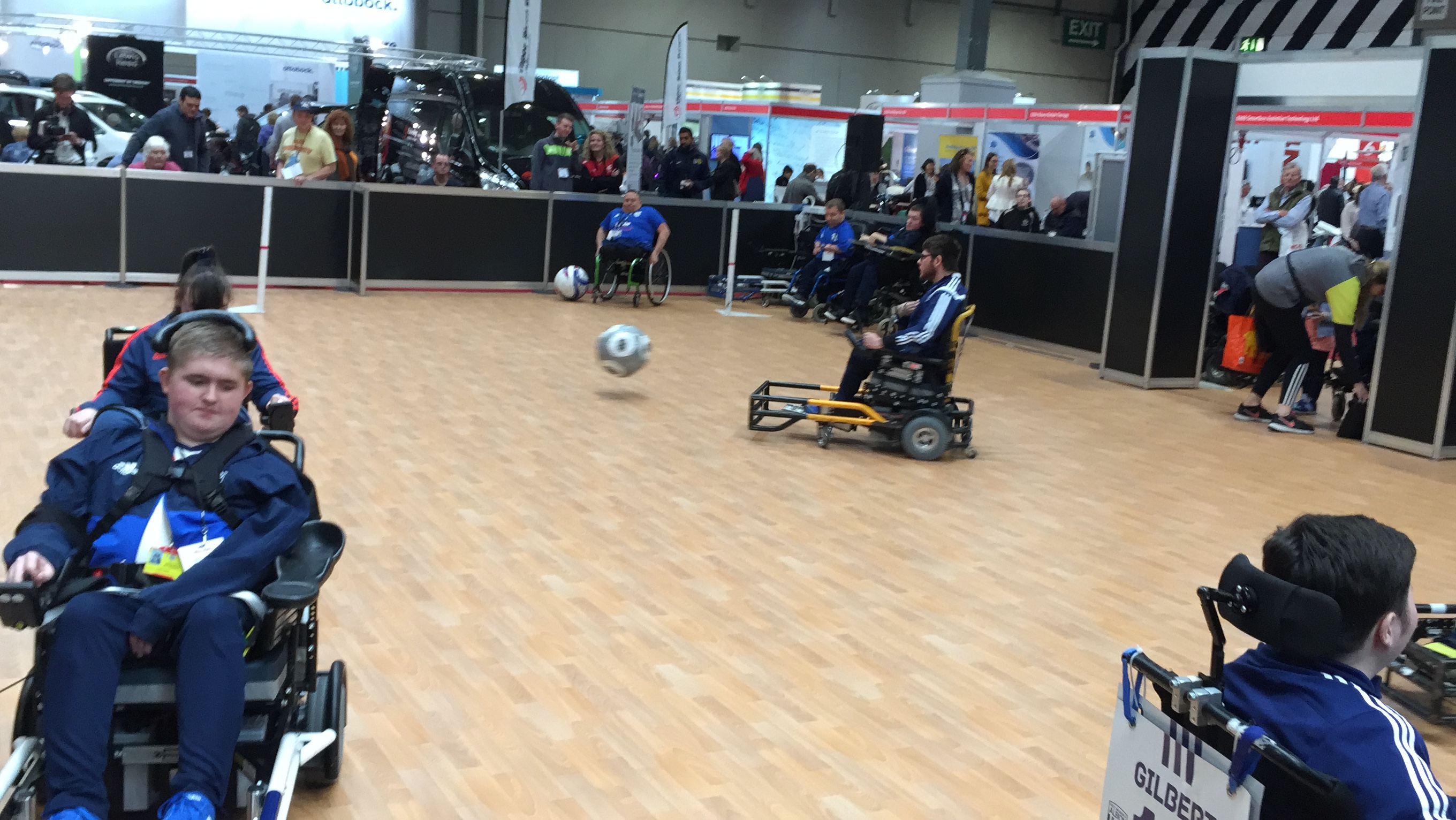 Powerchair Football at Naidex. The powerchairs have a an attachment made of thick bars on the front, which is used to kick the ball.