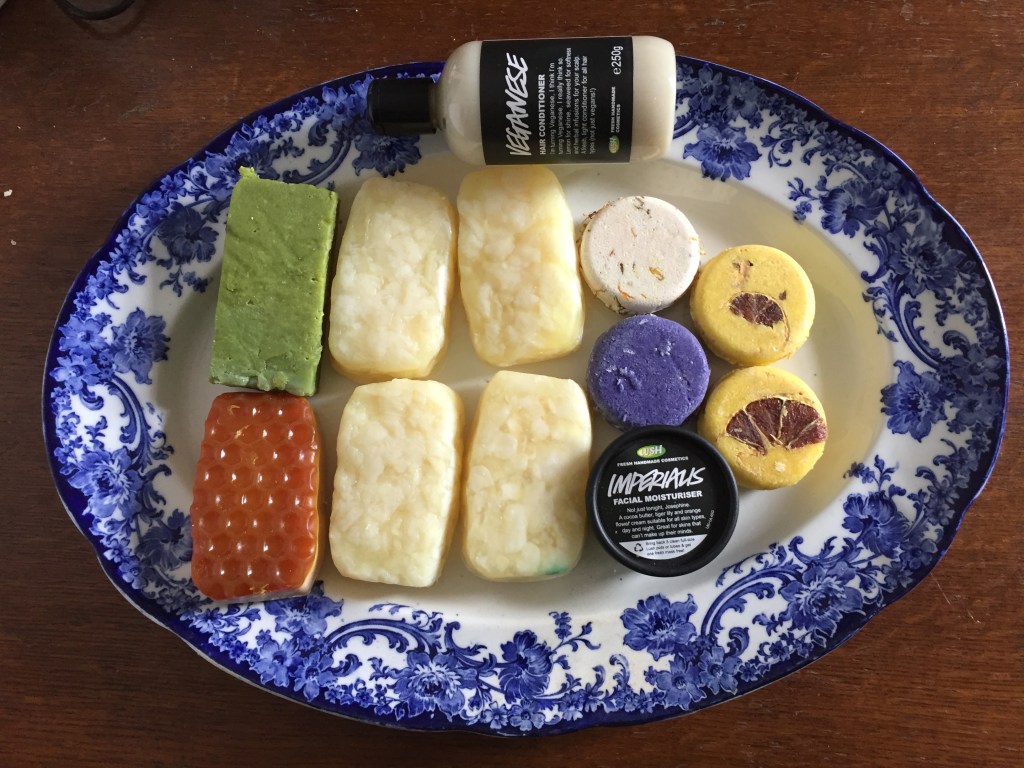 Large ornately decorated plate with the contents of our Lush order - 6 soap bars (including 4 Bohemian bars), 4 shampoo bars (including 2 Montalbano bars), a tub of Imperialis moisturiser, and a bottle of Veganese hair conditioner.