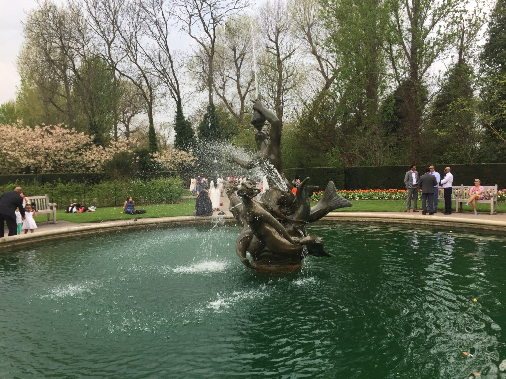The Triton Fountain in Regent's Park. In the centre of a round pool is a  group of bronze sculptures, depicting a sea god blowing on a conch shell with two mermaids at his feet.