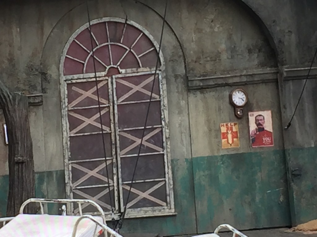 Close-up of the arched window at the back of the stage. On the wall next to it is a poster of Lord Kitchener pointing at the viewer, with the caption Your Country Needs You.
