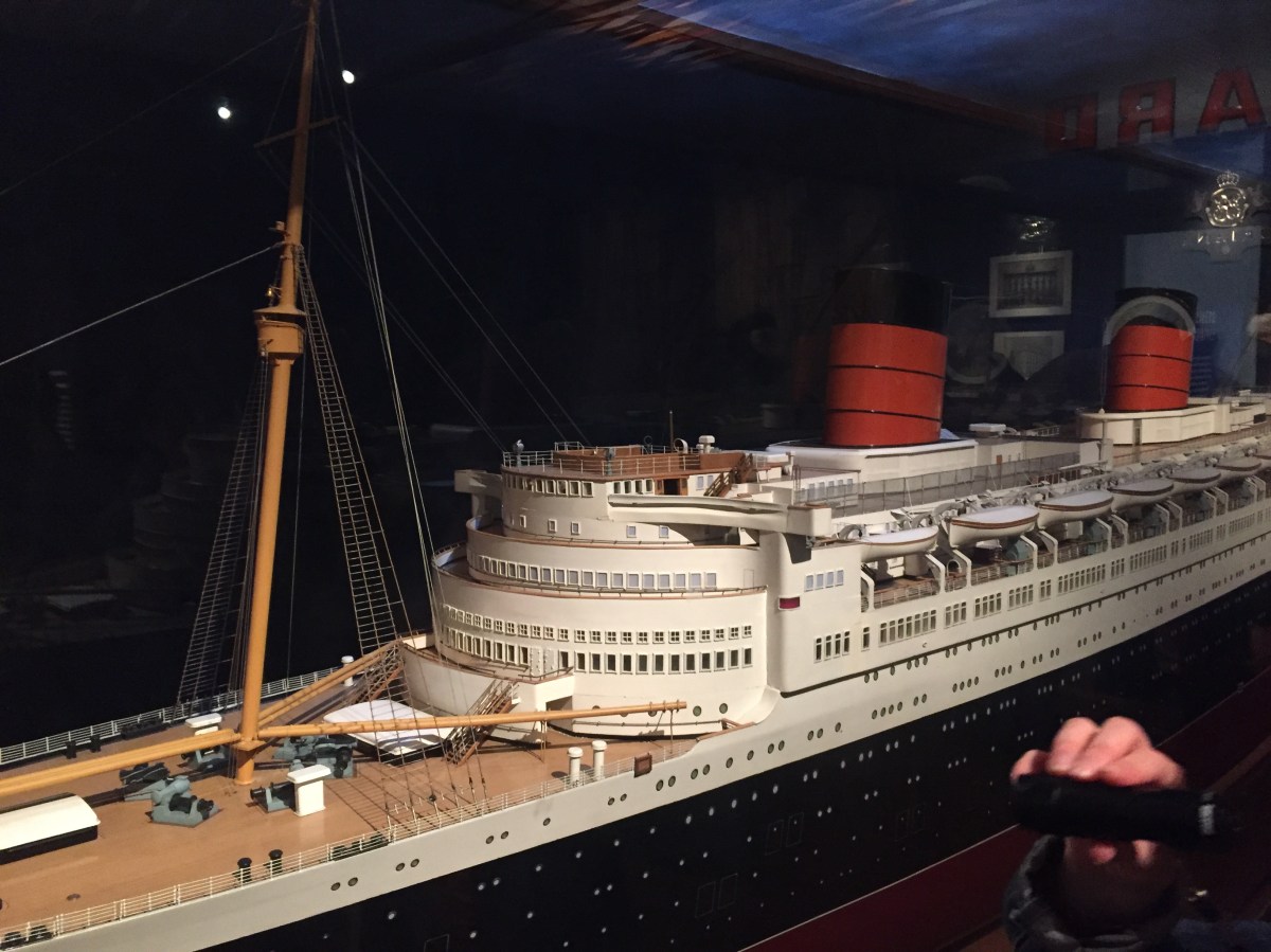 A very long and highly detailed model of the Queen Elizabeth Cruise Liner. The ship has a black base, with white buildings on the top, and details including the large mast down to the small lifeboats, windows and railings are all reproduced in the model.