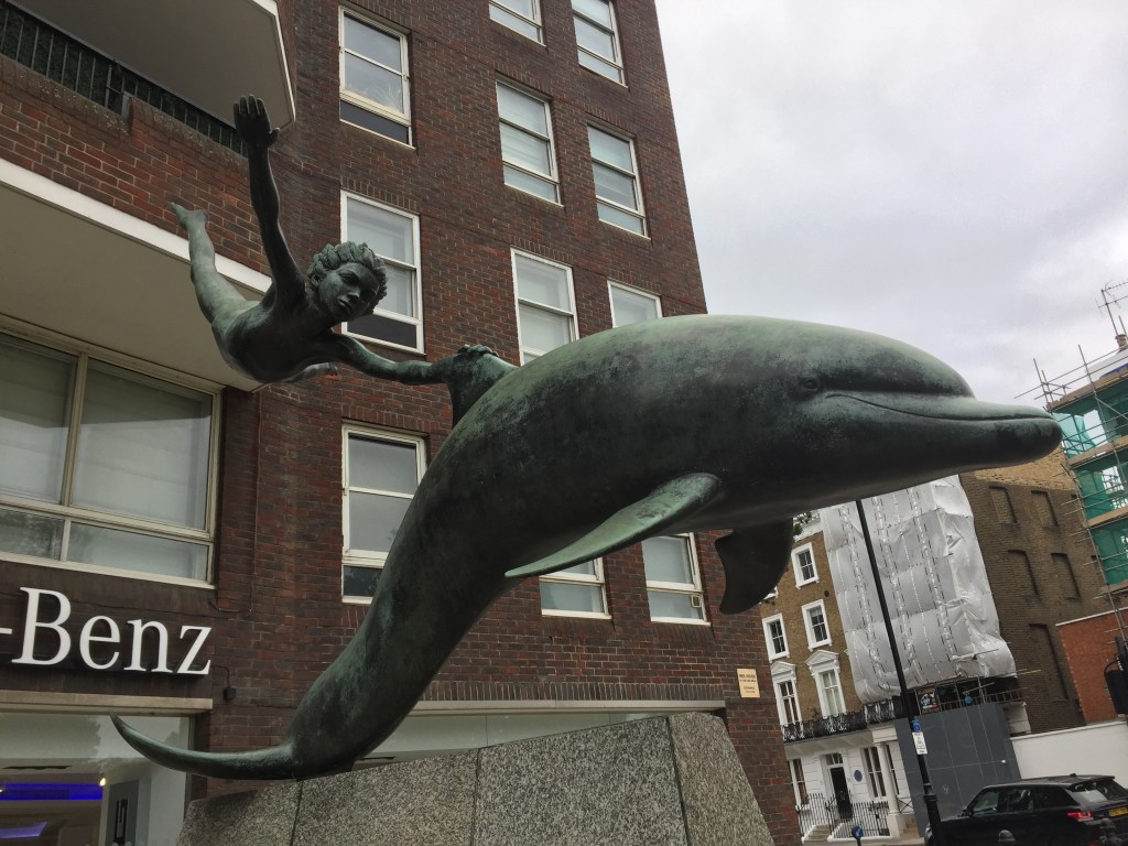 Statue of a dolphin swimming, with a boy clinging on to its upper fin as he floats in mid-air, giving the impression that the dolphin is moving at speed.