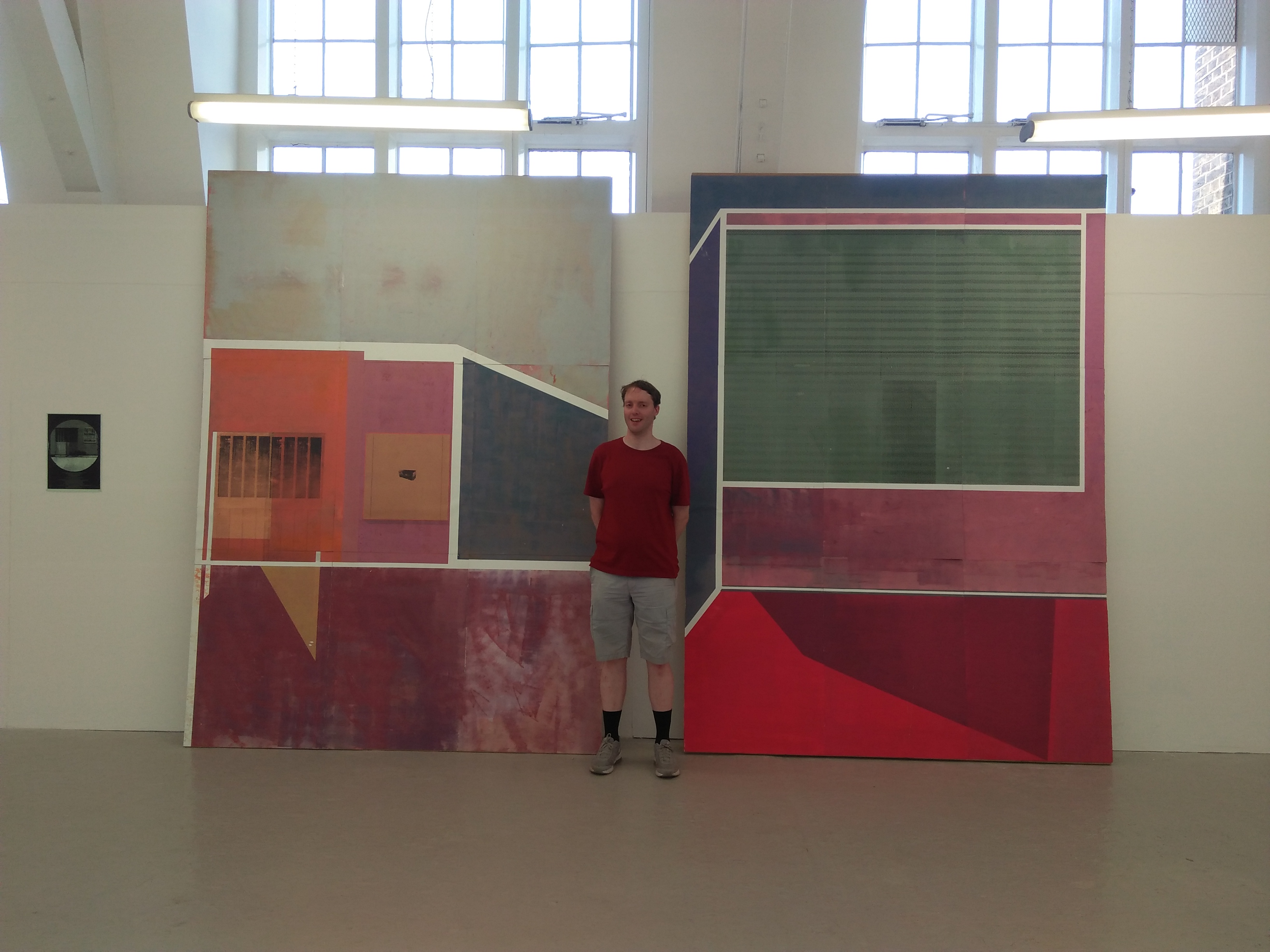 Me standing in front of a very large artwork, considering of large colourful panels, mainly squares and rectangles, but some have diagonal edges on one side.