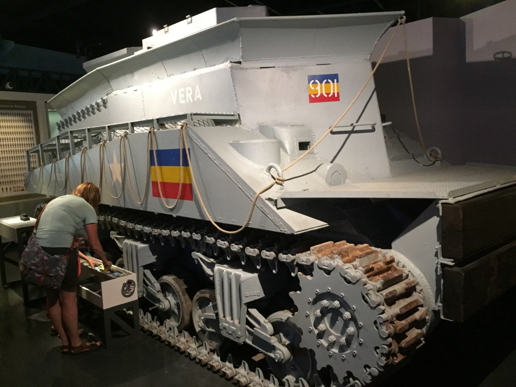 Huge grey tank in the D-Day Museum, A flag symbol on the side has 3 horizontal stripes of blue, yellow and red.