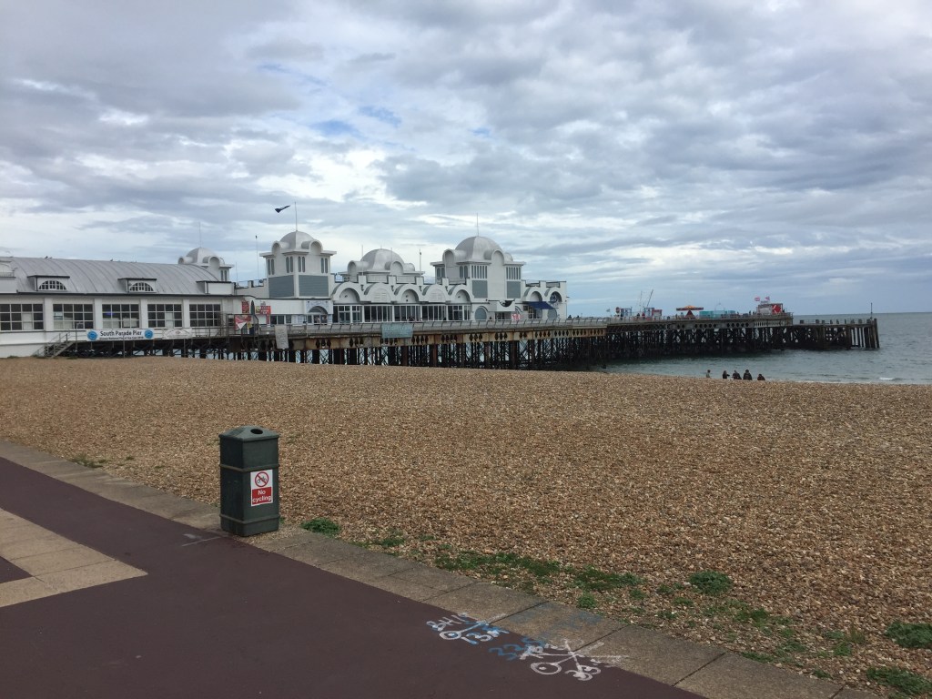 South Parade Pier, a long pier stretching out to sea. The white building on top, stretching from the shore to the centre of the pier, has a few arches on the side as part of its design.