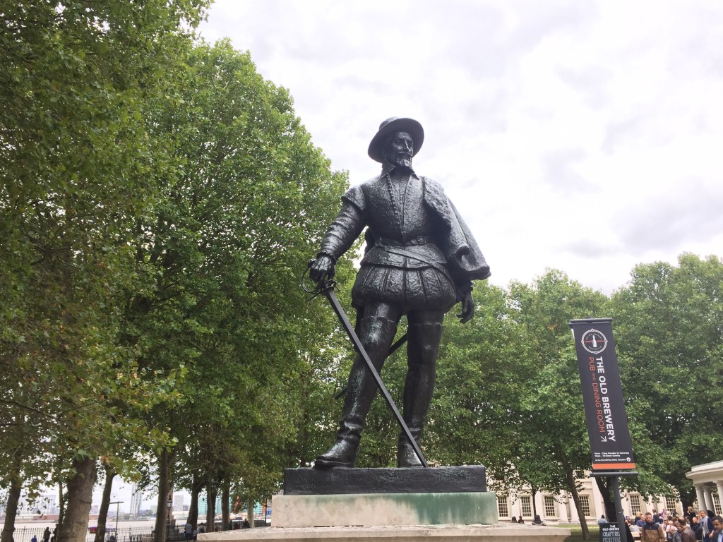 Statue of Sir Walter Raleigh, a bearded gentleman wearing a hat and a jacket that puffs out slightly around the waist, while holding a cane in his right hand that reaches down to his left food.