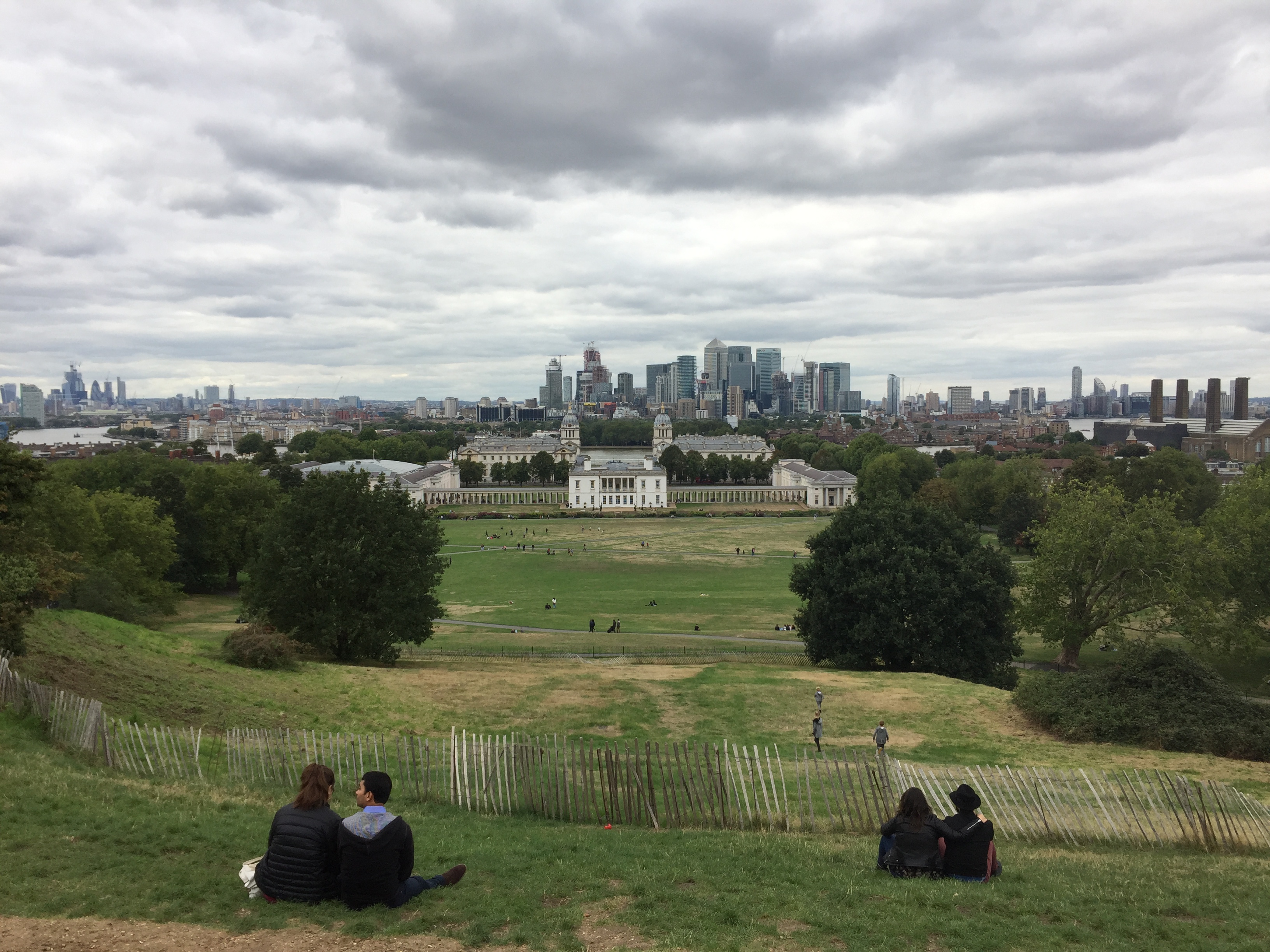 View of the London skyline from the top of a large grassy hill in Greenwich Park.