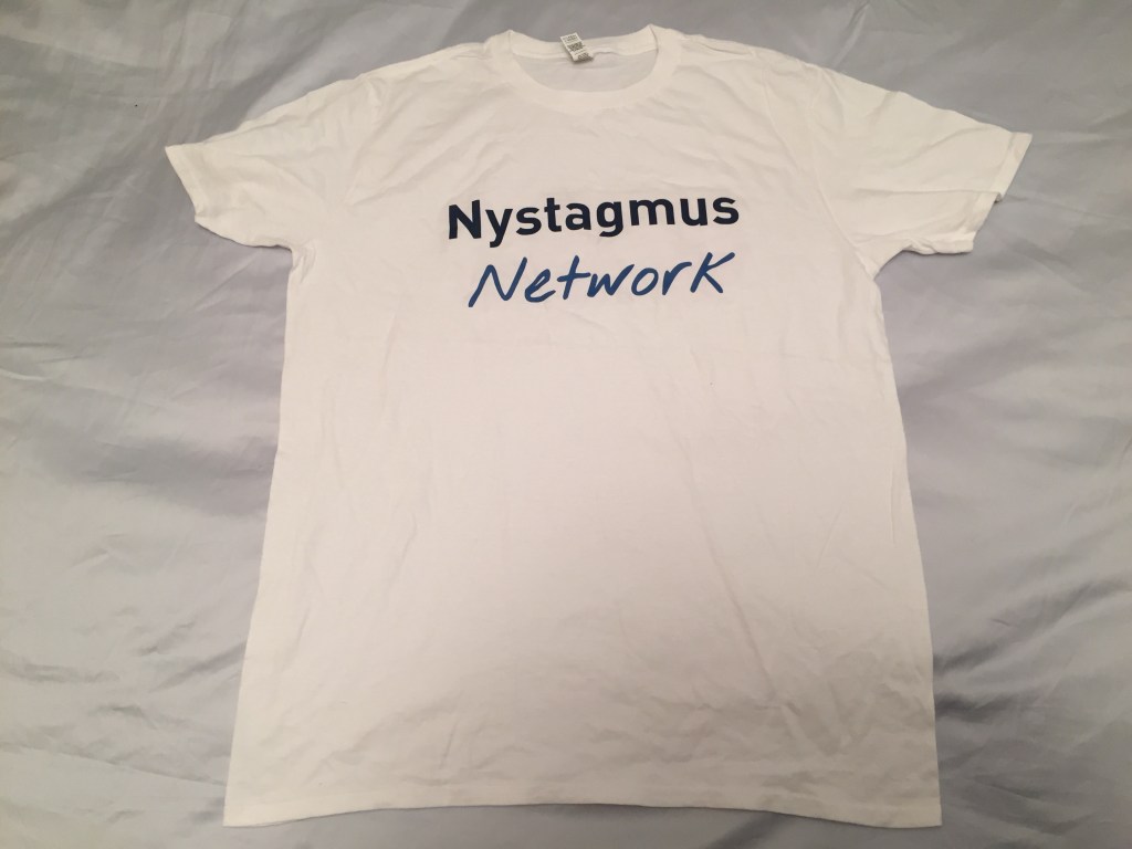 White t-shirt with the words Nystagmus Network near the top in blue lettering. The word Nystagmus is in a darker shade with typed letters, while the word Network is a lighter shade and in a handwritten style.