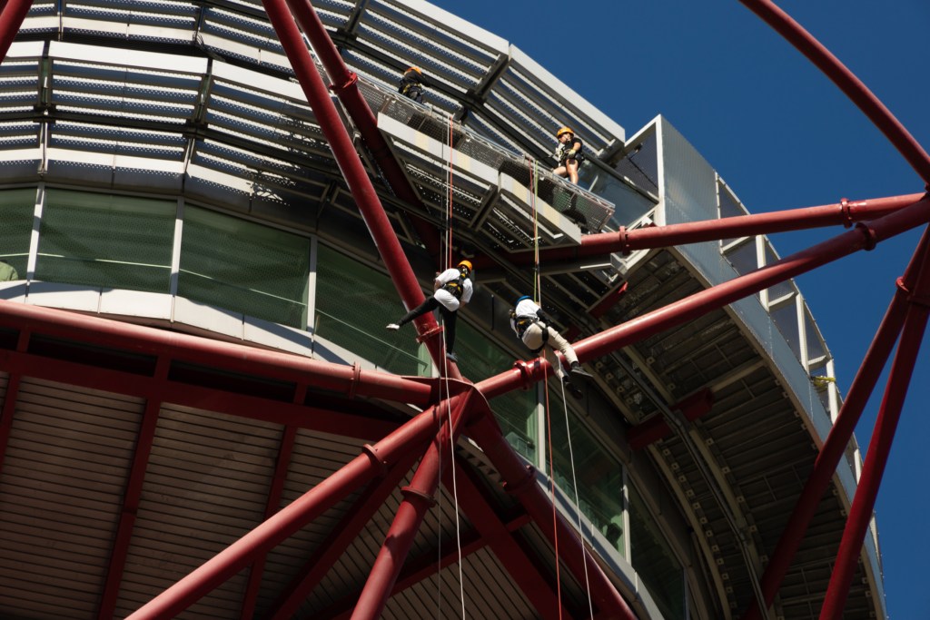 Photo by a spectator on the ground, zoomed in on Claire and Glen at the top of the tower, abseiling in mid-air a short distance below the platform.