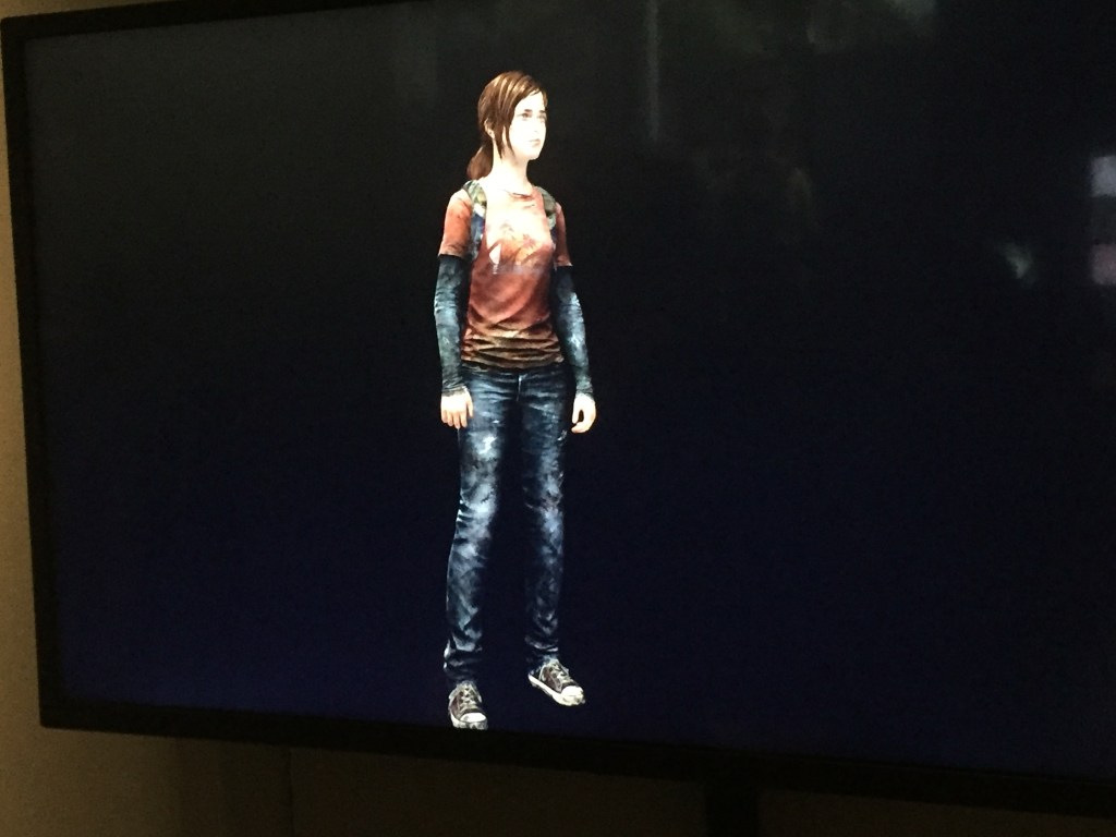 Rendered model of a character from the game The Last Of Us. She's wearing grey trainers with white toecaps and white laces, dark blue jeans with white patches, and a top that is mainly red but with arms a similar colour and design to the jeans. Her flowing brown hair reaches down to chin level on each side of her face.