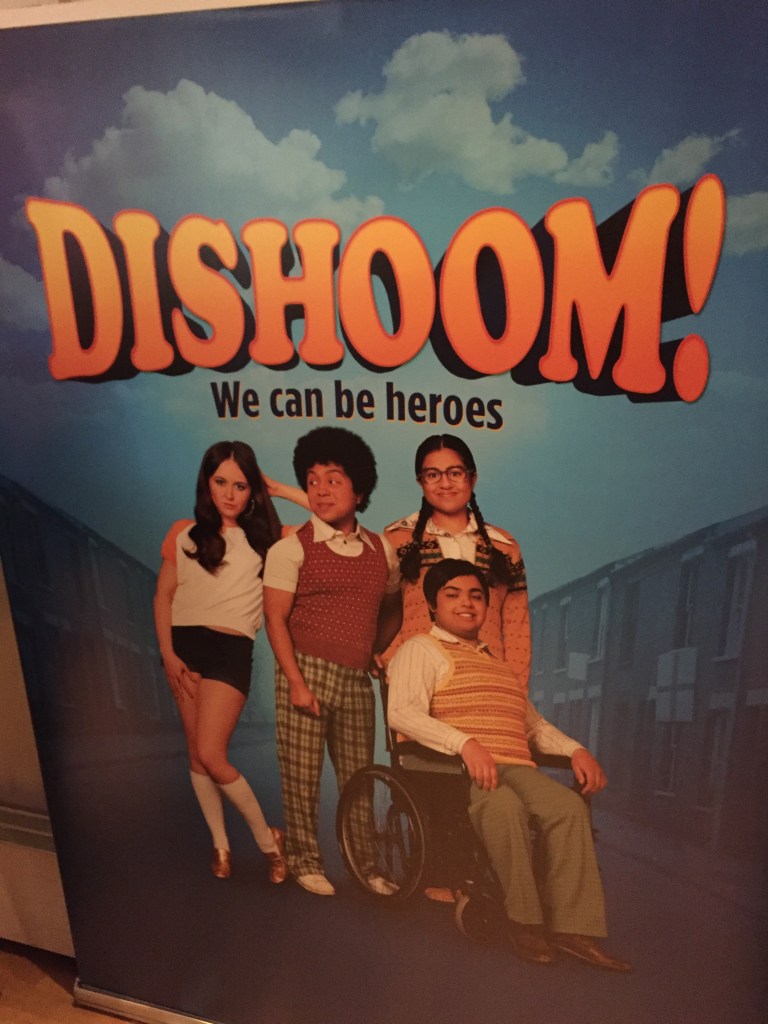 Poster for Dishoom!, with the strapline We Can Be Heroes. Below the text is a picture showing the main character, a young man in a wheelchair, with 3 of his friends behind him (1 male and 2 female).