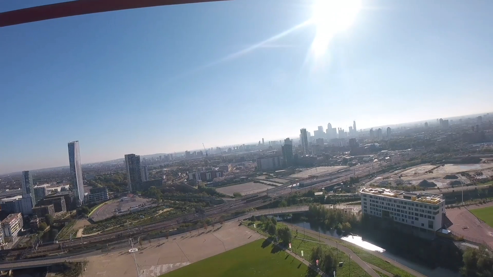 Headcam view of the Olympic Park and the London skyline, stretching far into the distance, beneath a clear blue sky with bright sunshine.