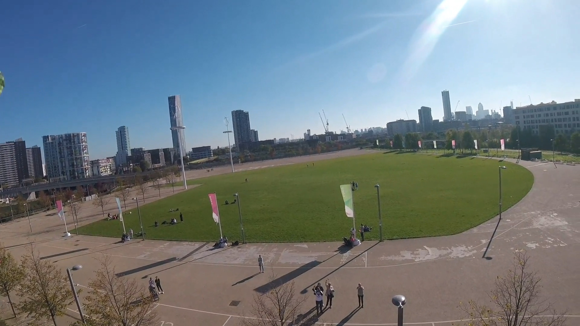 Headcam view of the large round grassy spectator area from a slightly lower angle. This time, on the large concrete area surrounding the grass, a few friends can be seen looking up and waving at the bottom of the photo.