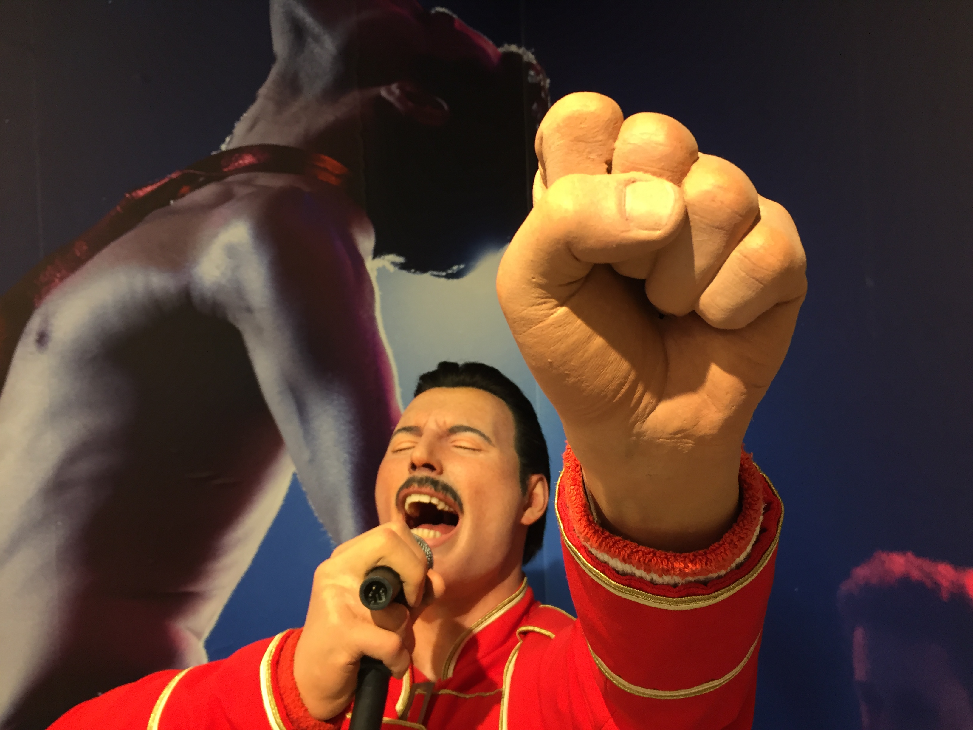 Close-up of the Freddie Mercury statue, with Freddie's fist punching the air close to the camera, as he sings powerfully in the background.