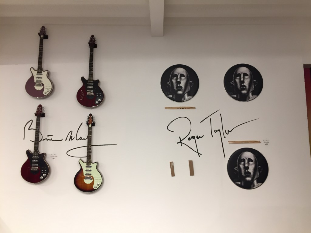 Wall display in the Queen shop with 4 electric guitars signed by Brian May, and drumsticks from roger Taylor.