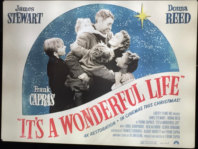 Movie poster for It's A Wonderful Life, starring James Stewart and Donna Reed. The large central image shows the family from the movie in a group embrace, with the mother, father and three children. They are shown in black and white, as in the film, but are on a blue background with snow falling around them. Below the movie's title is text saying 4K restoration, in cinemas this Christmas.
