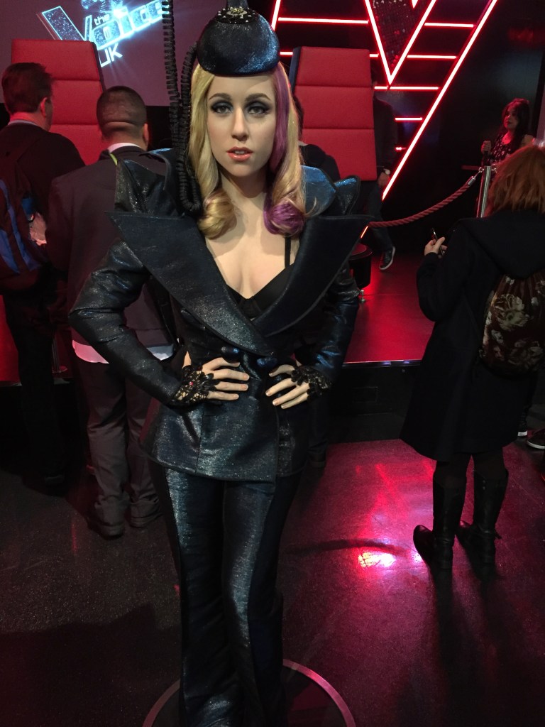 Waxwork of Lady Gaga at Madame Tussauds. She poses with her hands on her hips, wearing a black leather jacket and trousers that shine in the light.