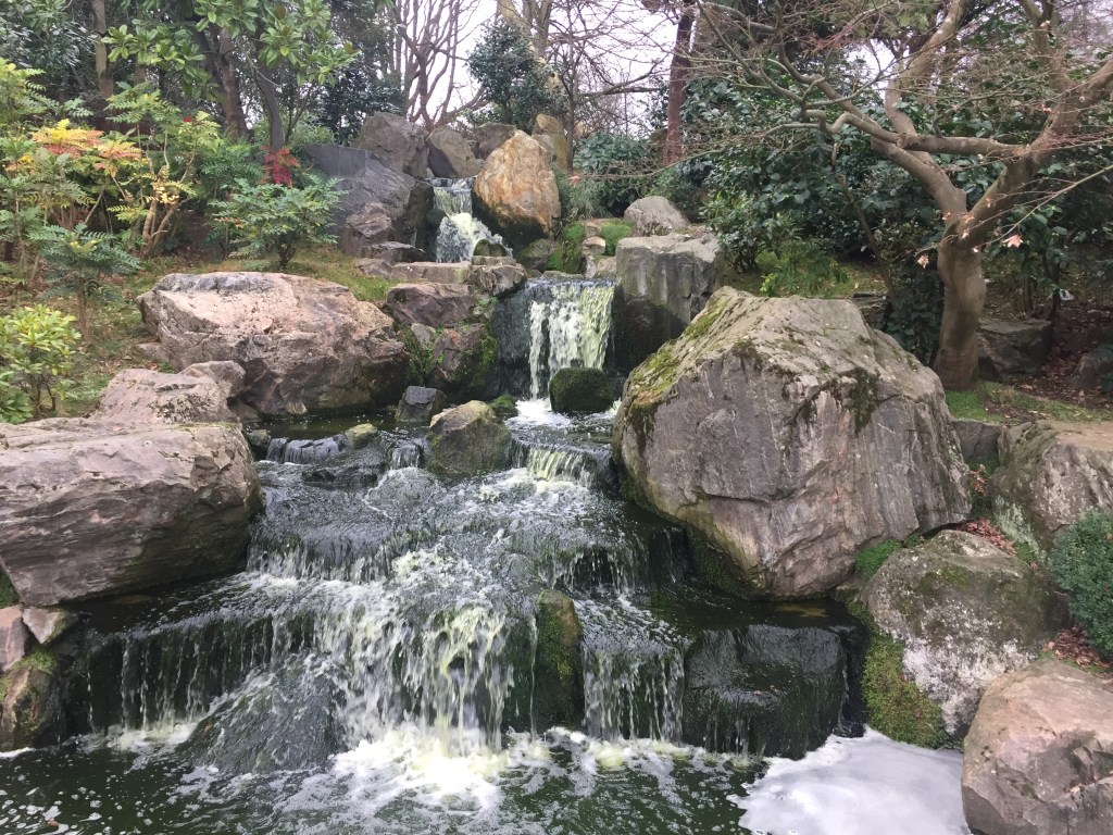 A small waterfall flowing over rocks into a pool below.
