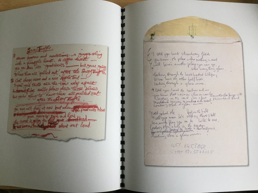 2 pages from the book for the White Album box set, each showing a colour photograph of a piece of paper with handwritten lyrics on it. The central spine between the pages is printed all the way down with small black blocks so that it looks like a binder.