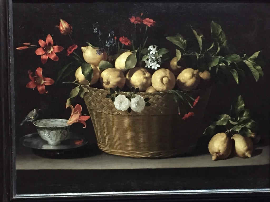 Still life painting. In the centre is a large woven basket filled with fresh lemons, along with sprigs of lemon blossom, red carnations, blue delphiniums, two white roses, day lilies and a tulip. in the bottom left is a silver bowl filled with water, on a blue-and-white porcelain bowl. A goldfinch perches on the lip of the bowl, and a day lily floats in the water.