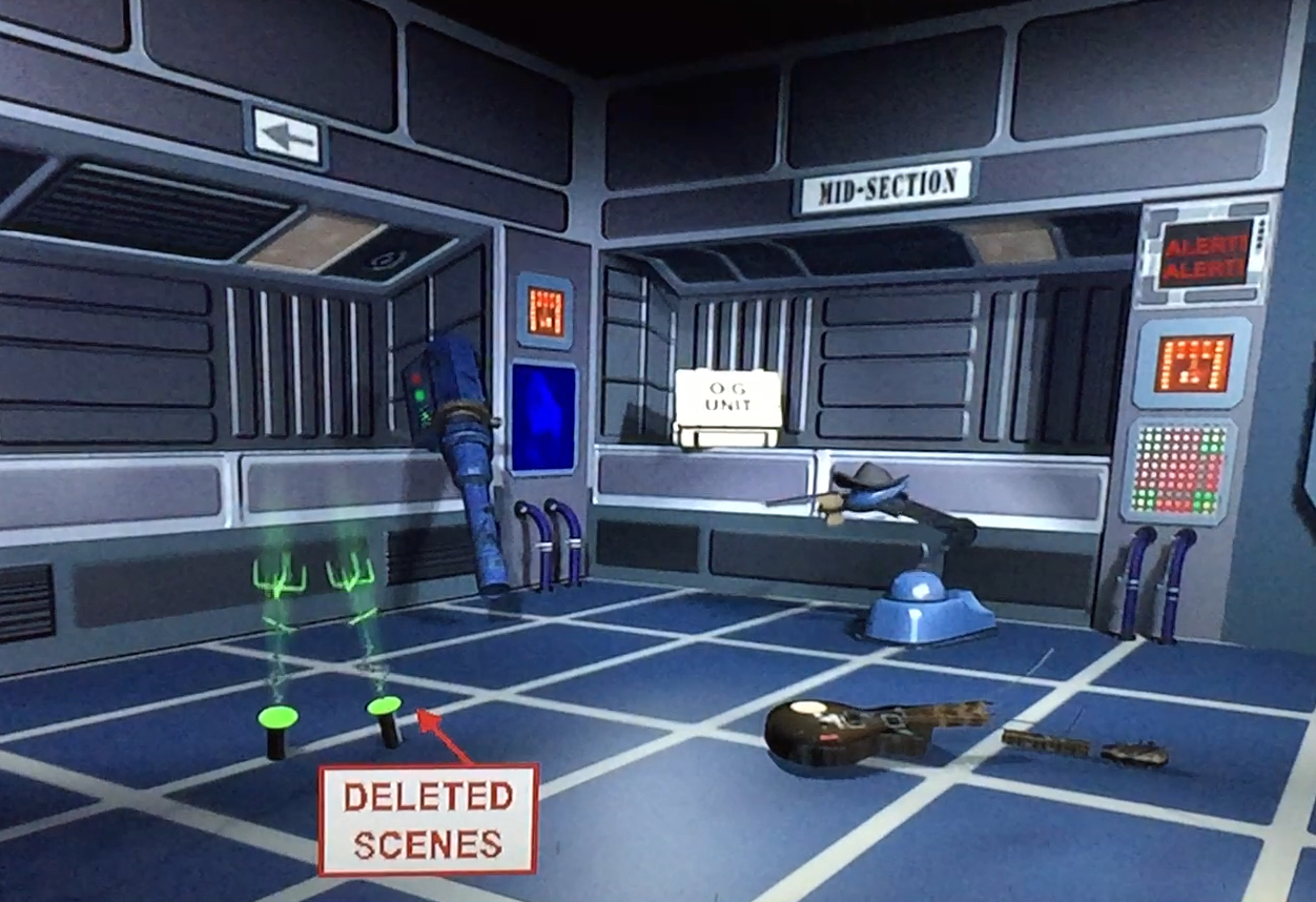 The extras DVD menu for Red Dwarf series 6. The screen shows a room with metal walls, some panels of buttons, and a floor made of blue squares with white borders. Moving around the screen allows you to select various items to access different features, including a broken guitar, a skutter robot and a bazookoid gun.