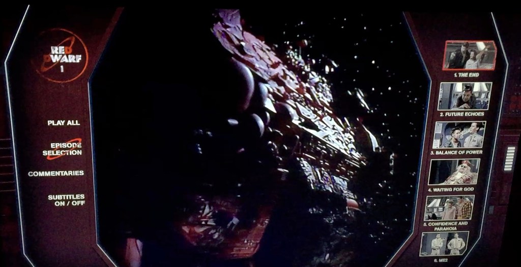 Menu for the Blu-ray of Red Dwarf series 1. In the centre of the screen is an image of the huge Red Dwarf spaceship flying through space. To the left, in white text on a dark background, are options for Play All, Episode Selection, Commentaries and Subtitles. On the opposite side of the screen, again in white on black, is the list of episodes, with each represented by a thumbnail image from the show, as well as the episode number and title.