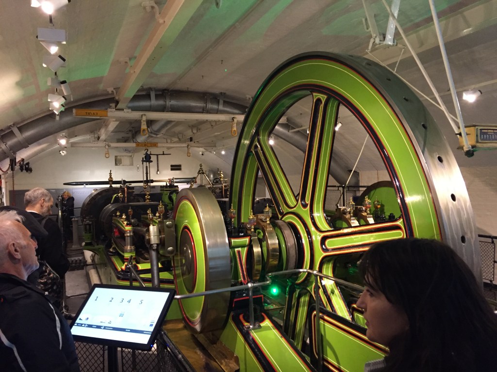 Machinery in the engine room under Tower Bridge, driven by a very large green wheel.