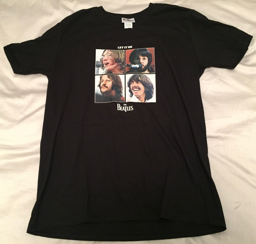 Black T-shirt featuring a grid of 4 photos of the members of The Beatles. Above the photos in white text is the wording Let It Be, while below the photos is the band's logo.
