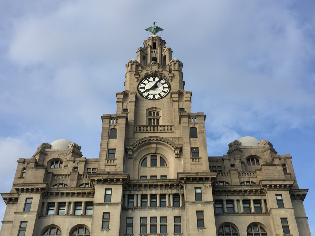 The spire of the Royal Liver Building, with a black and white clock face on the front, and a statue of a bird with outstretched wings standing on the very top of the spire.