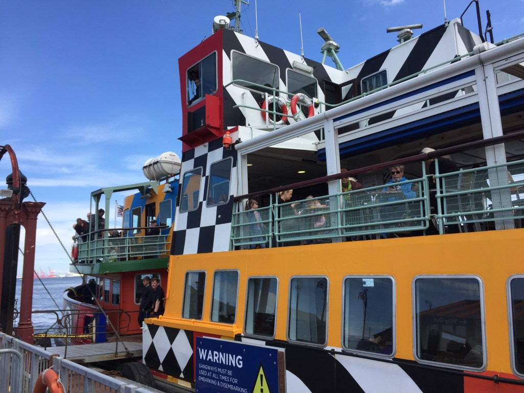 The colourful Dazzle Ferry boat, with bold, striking patterns in yellow and blue, along with large checkerboard patterning and wide diagonal stripes in black and white.