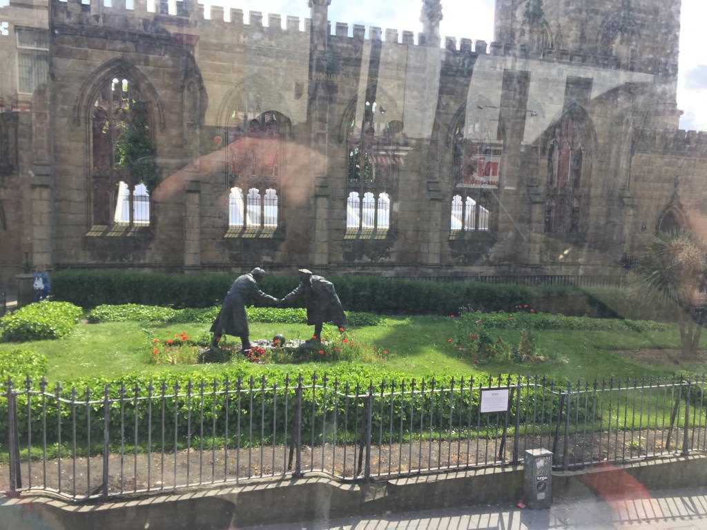 The Christmas Truce statue on a patch of grass outside the Bombed Out Church in Liverpool. The statue, called All Together Now, shows 2 soldiers facing each other as they shake hands, with a football on the ground between them.