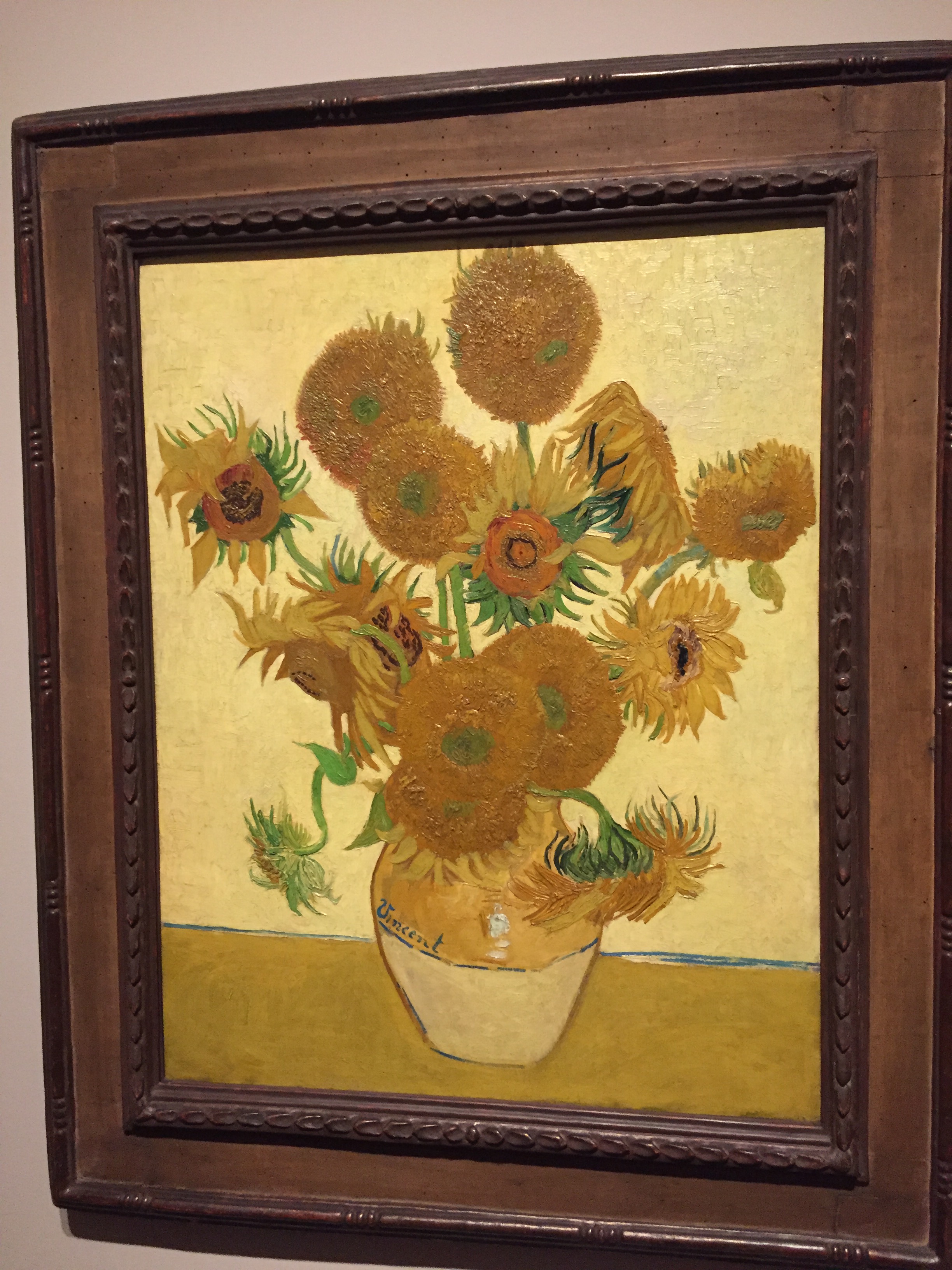 Sunflowers painting by Vincent Van Gogh, showing a small vase holding a big bunch of sunflowers, some of which are in bud, some of which are fully open, and some of which appear to have died.