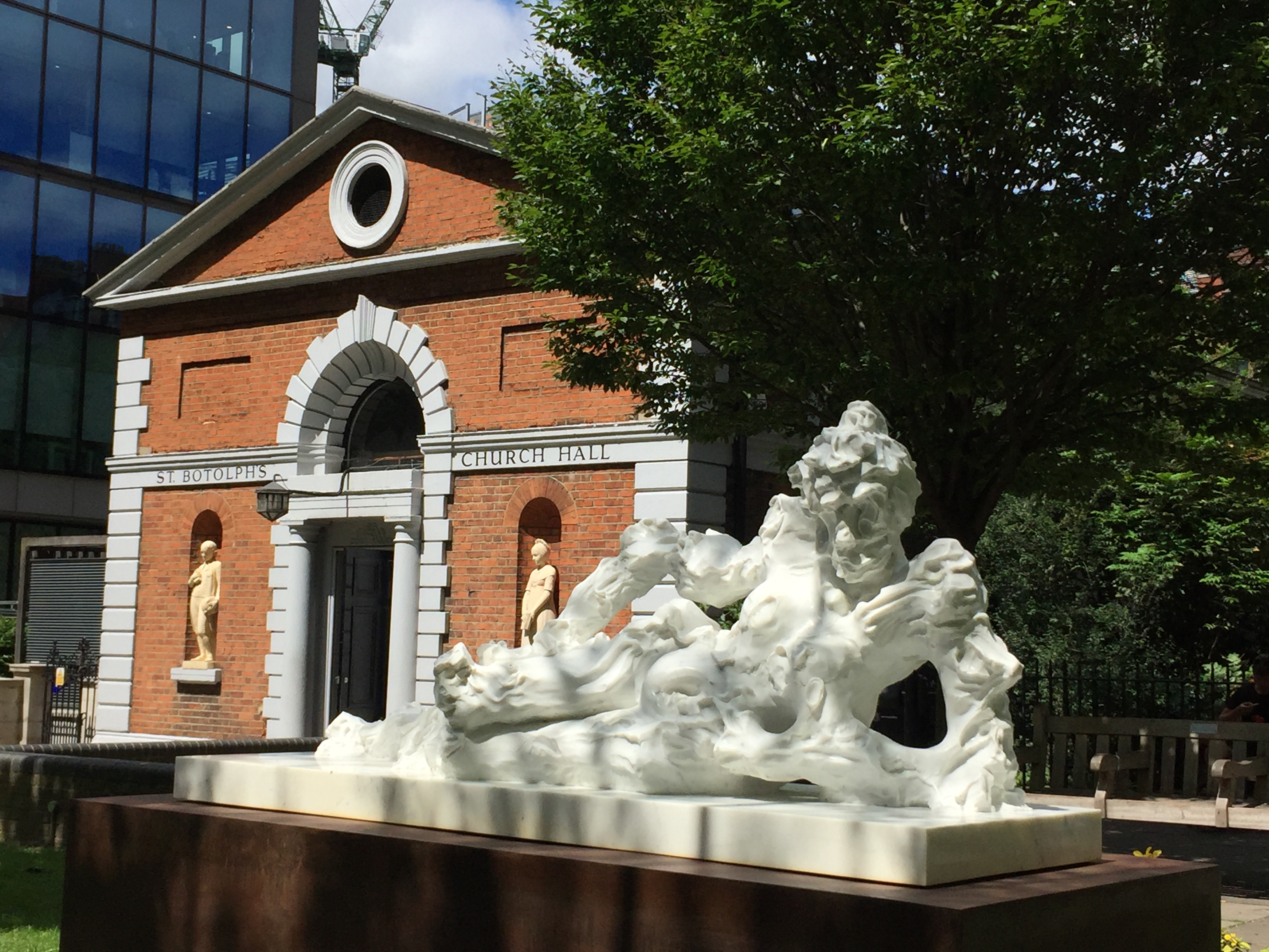 A white marble statue resembling the figure of a nude lady, propping herself up on her left elbow as she rests on her side looking at us. The marble is sculpted in an apparently messy and lumpy way, howeer, giving a very distorted appearance to the figure.