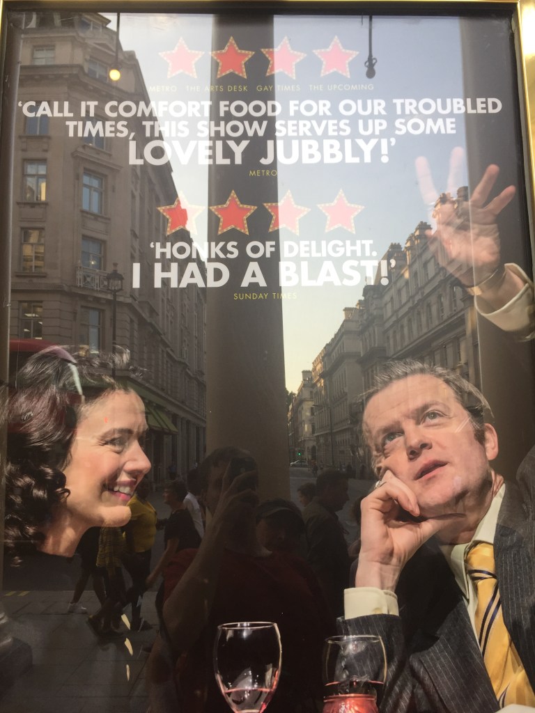 Poster for the Only Fools And Horses musical, showing Raquel and Del Boy sharing drinks on a date. Above them are a couple of review quotes. Metro says Call it comfort food for our troubled times, this show serves up some lovely jubbly! The Sunday times says Honks of delight, I had a blast!