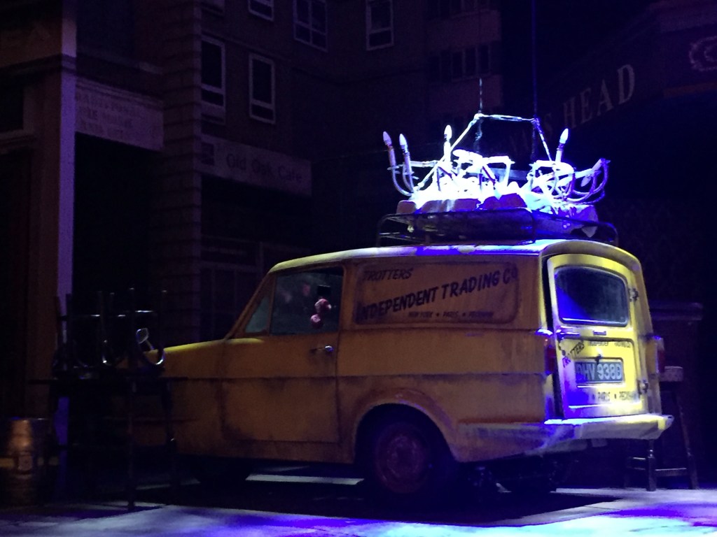The yellow three-wheeled Reliant Regal van used by the Trotter family, parked on stage at the Only Fools And Horses musical.The words Trotters Independent Traders, New York, Paris, Peckham are written in black on the side, while a smashed chandelier sits on the roof.