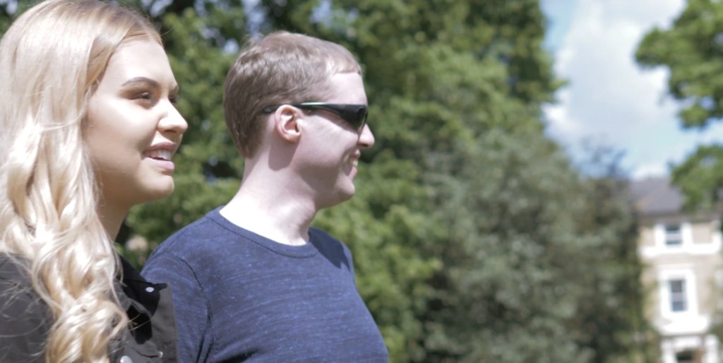 Amy and Glen standing and smiling together in the park in the sunshine.