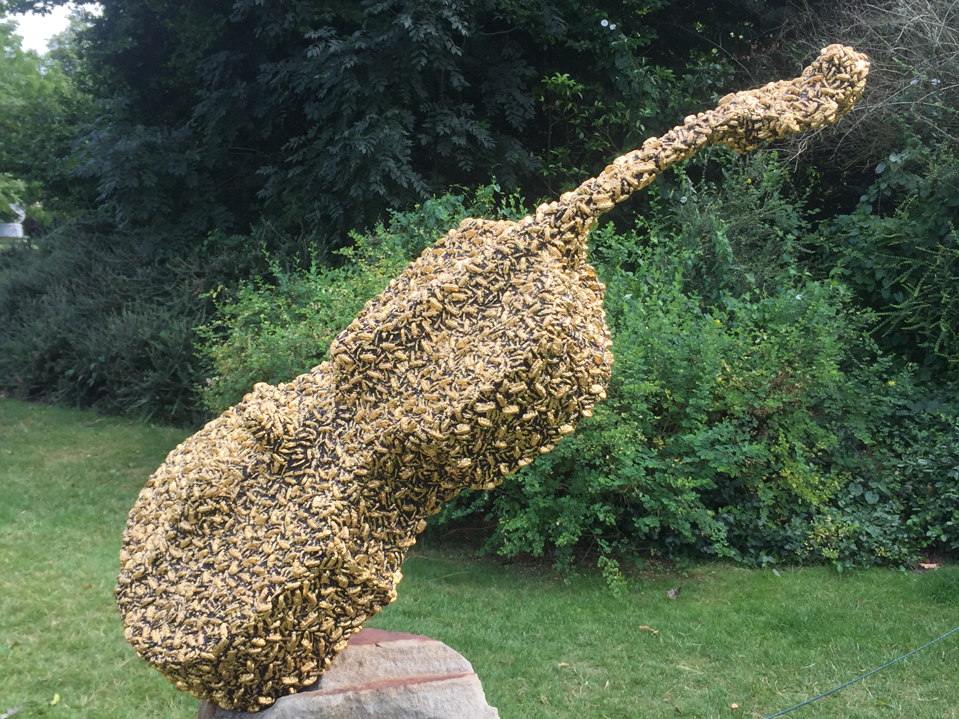 Sculpture of a cello completely covered in a swarm of bees.