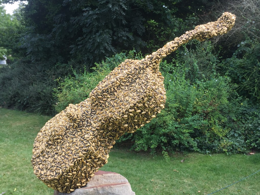 Sculpture of a cello completely covered in a swarm of bees.