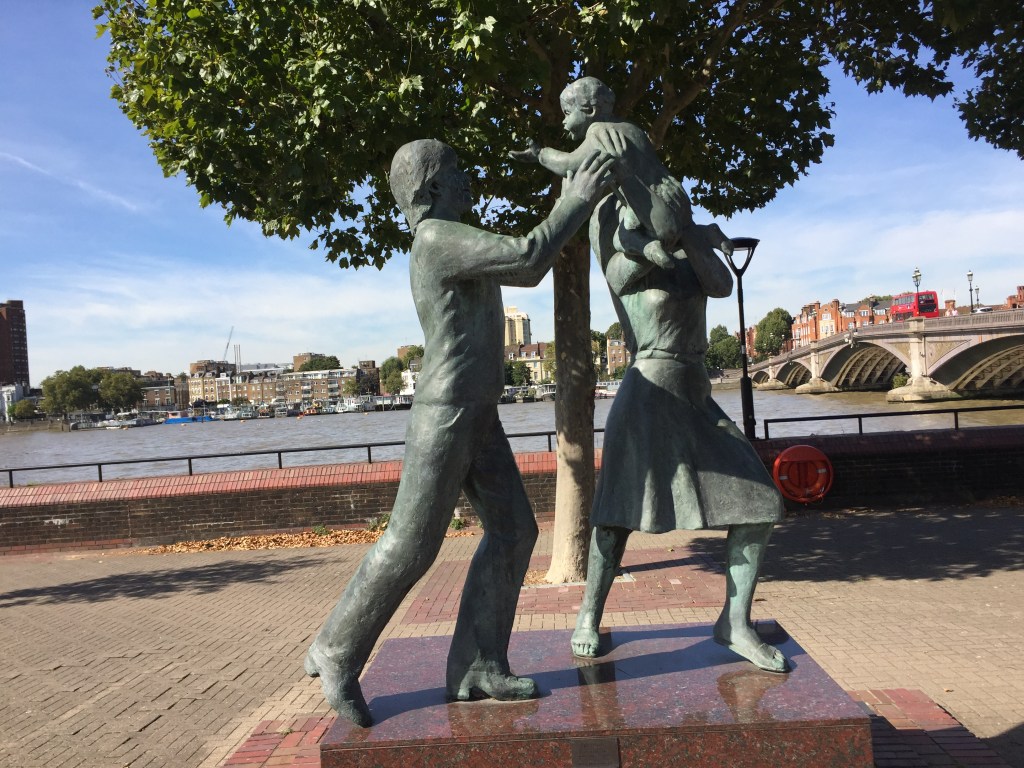 Statue of a man and and a woman holding a smiling baby up in the air between them.