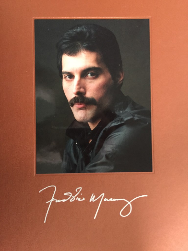 Head and shoulders photo of Freddie Mercury wearing a leather jacket, above his signature in silver writing, from the cover of the book in his Solo Collection box set.