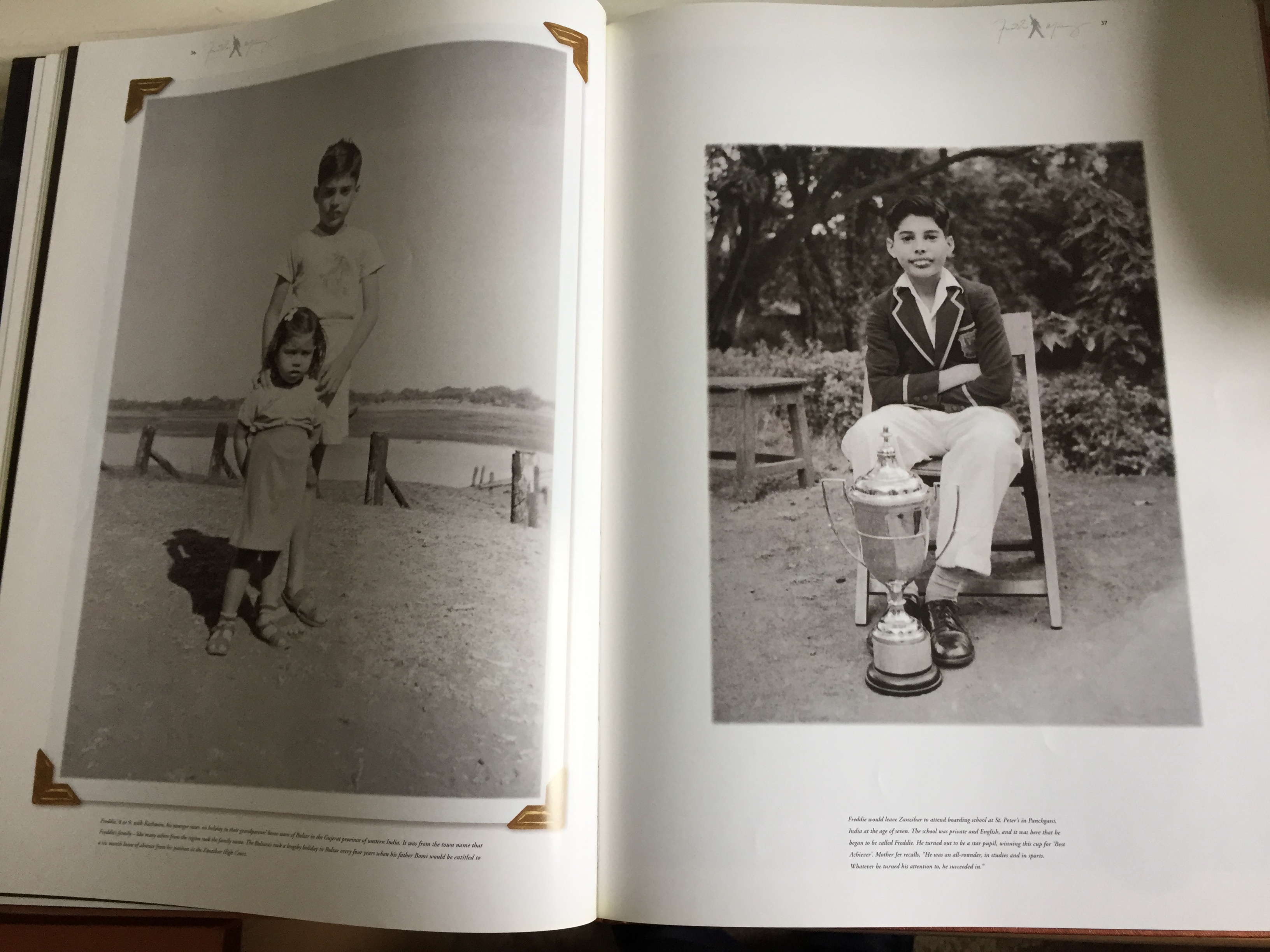 Pages from the Freddie Mercury Solo Collection book, showing photos of the star as a child, one showing him standing tall behind his younger sister, and the other showing him sitting on a chair and smiling with a large trophy on the ground in front of him.