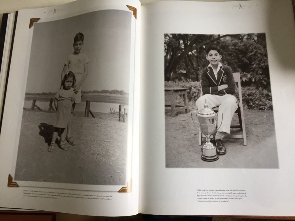 Pages from the Freddie Mercury Solo Collection book, showing photos of the star as a child, one showing him standing tall behind his younger sister, and the other showing him sitting on a chair and smiling with a large trophy on the ground in front of him.