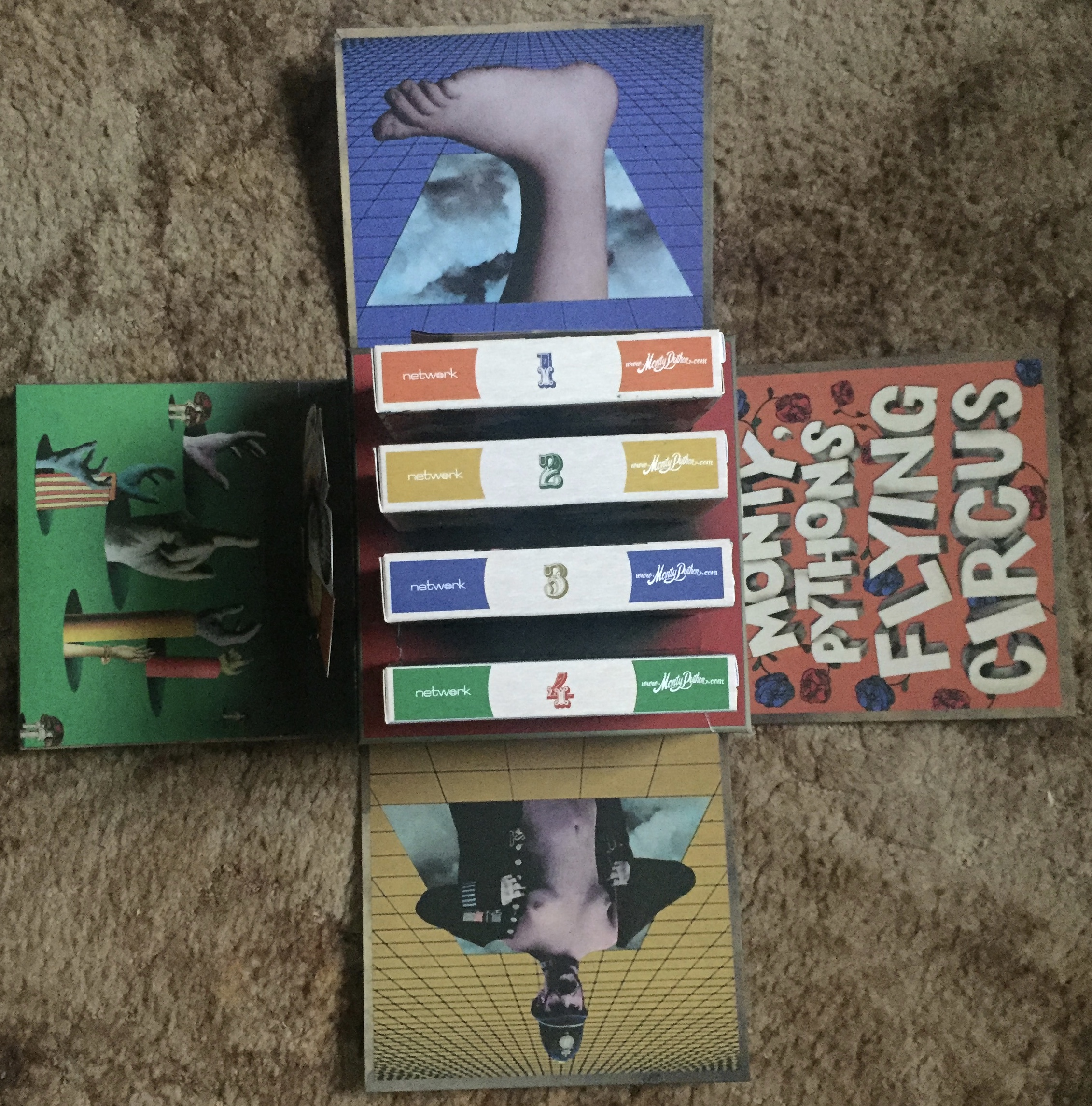 The open box for the Monty Python 50th Anniversary Blu-ray box set. All 4 sides of the cube are spread out on the floor, each with imagery from the show, while in the centre of the box are cases for each of the 4 series.