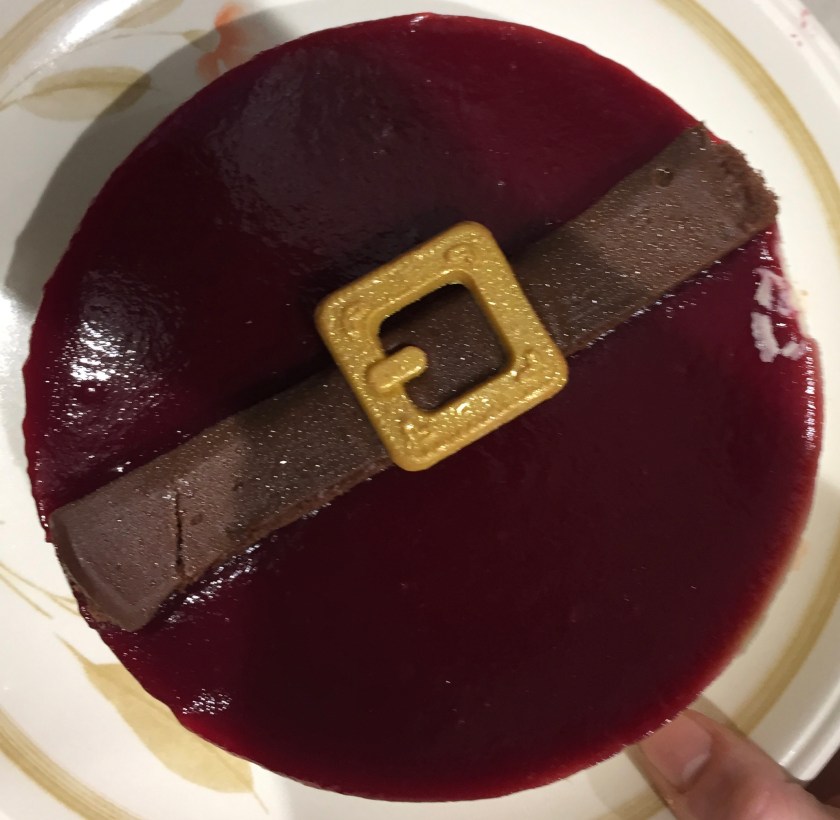 Santa's Raspberry Belly Cheesecake from Sainsbury's. A thick layer of raspberry sauce covers the top of the cheesecake, and is overlaid by a chocolate belt and an edible golden buckle.