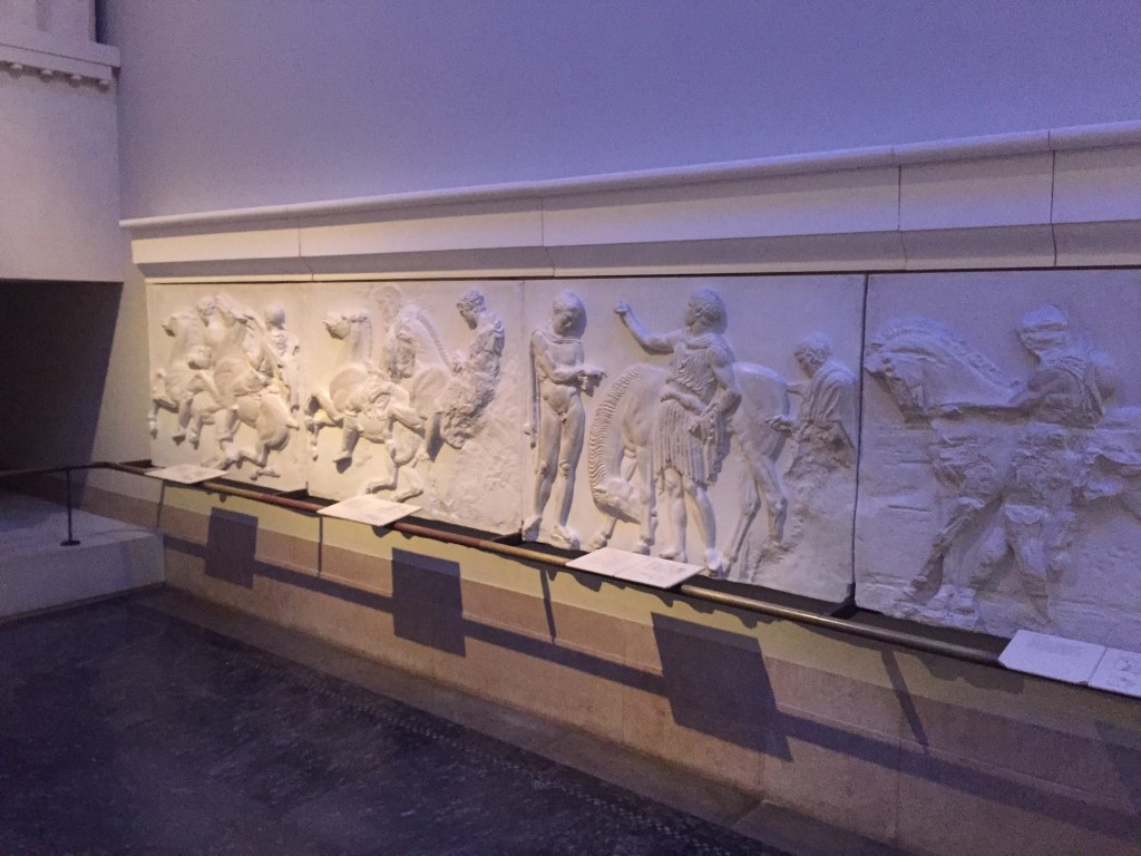 Lifesize tactile cast replica of part of the sculptural frieze from the Parthenon, showing a variety of people, some on horseback and some standing.
