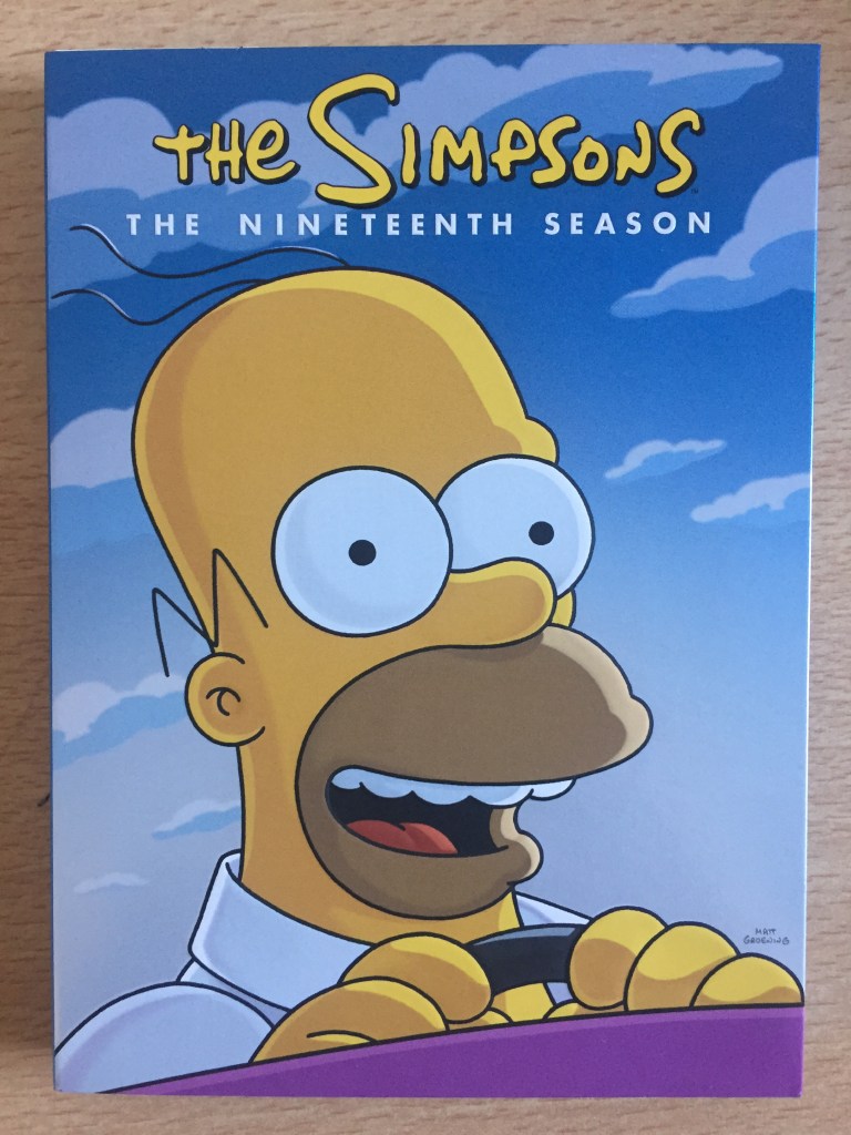 Front cover of the DVD box set for The Simpsons Season 19, showing Homer smiling as he drives his car.