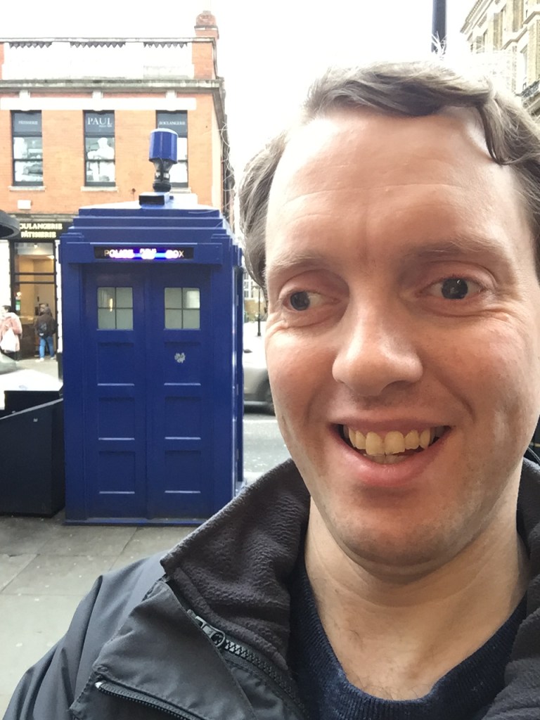 Selfie of Glen smiling, in front of a big blue police phone box that looks like Doctor Who's Tardis.