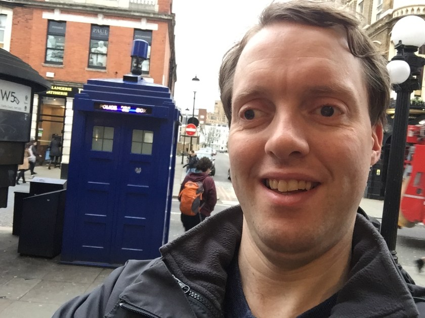Selfie of Glen smiling, in front of a big blue police phone box that looks like Doctor Who's Tardis.