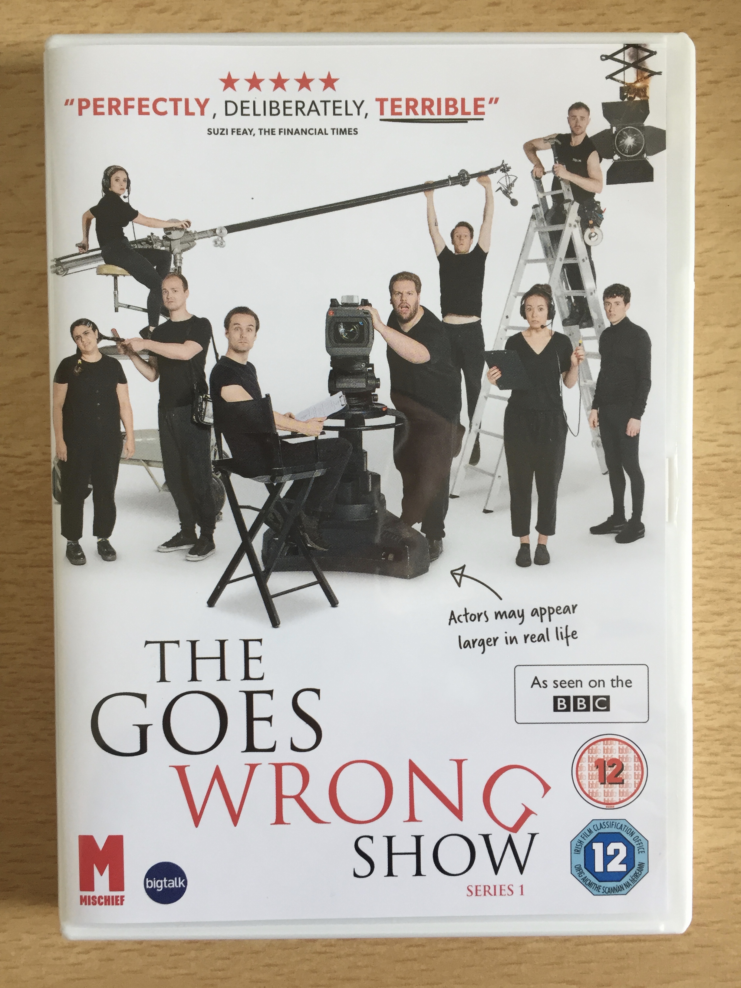 DVD cover for The Goes Wrong Show, series 1, showing the cast posing with filming equipment, including a camera, an overhead boom microphone and lighting.
