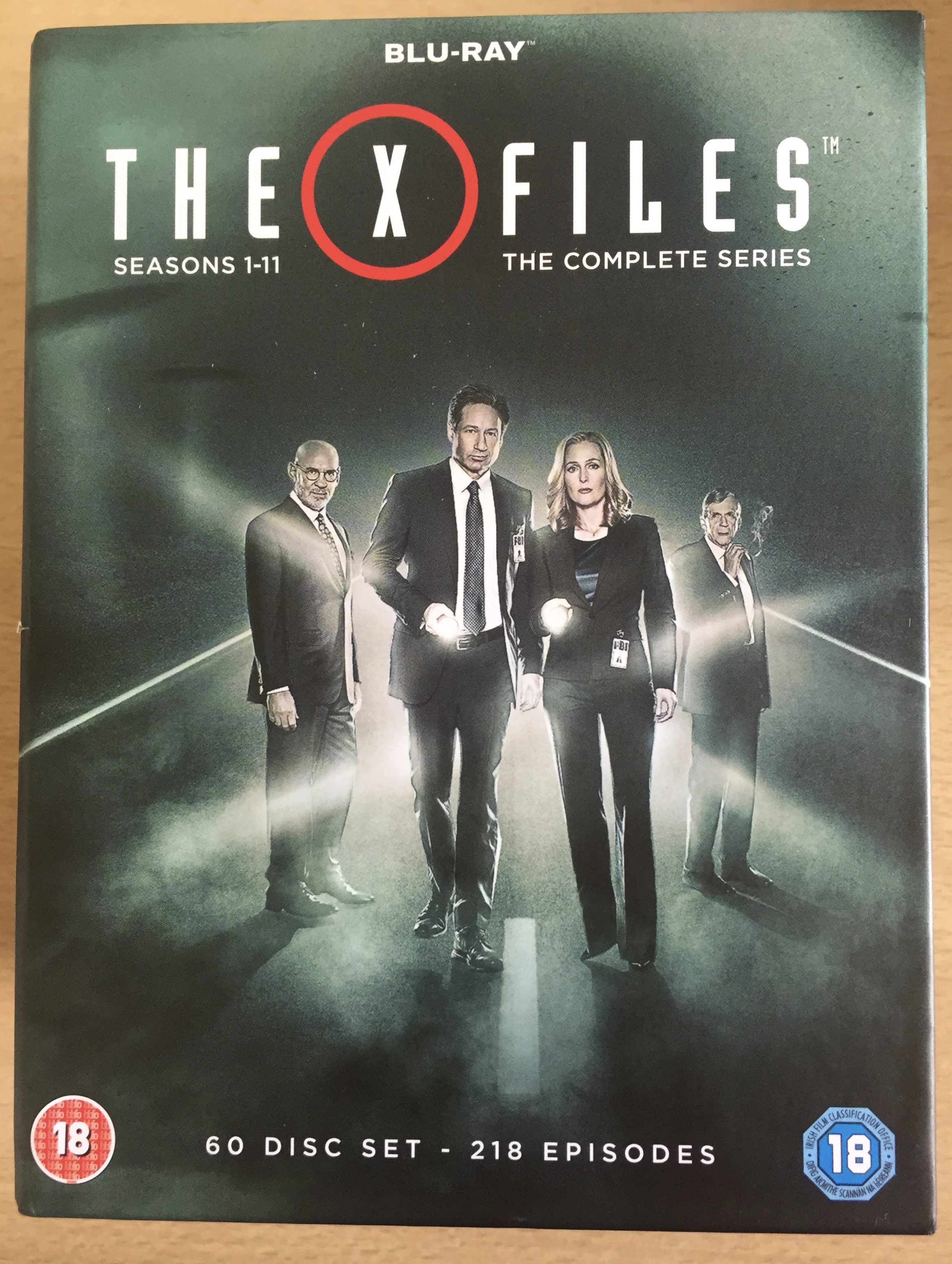 Cover for the Blu-ray set of The X Files, with all 11 seasons, 218 episodes, on 60 discs. The image shows Mulder, Scully, Skinner and the Cigarette Smoking Man in front of a bright light.